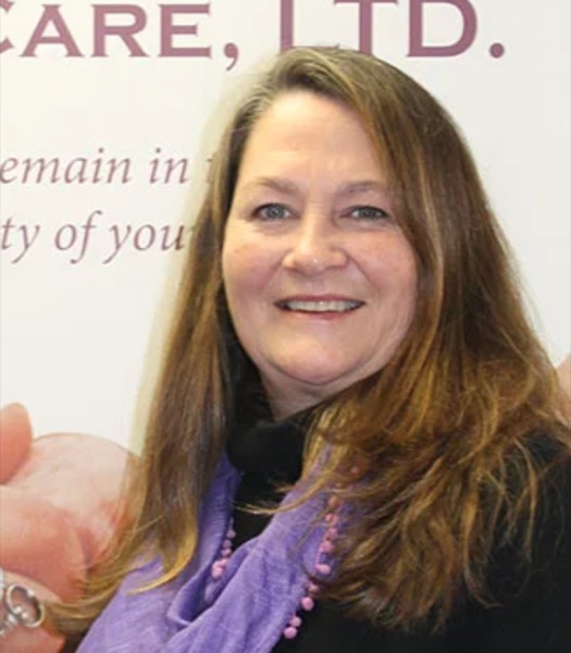 Kim Sloane smiling in a purple scarf, standing in front of a Human Touch Home Care banner